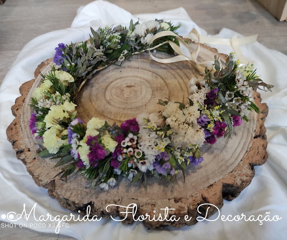 Coroa de flores naturais e secas coloridas sobre tronco de madeira rústica
