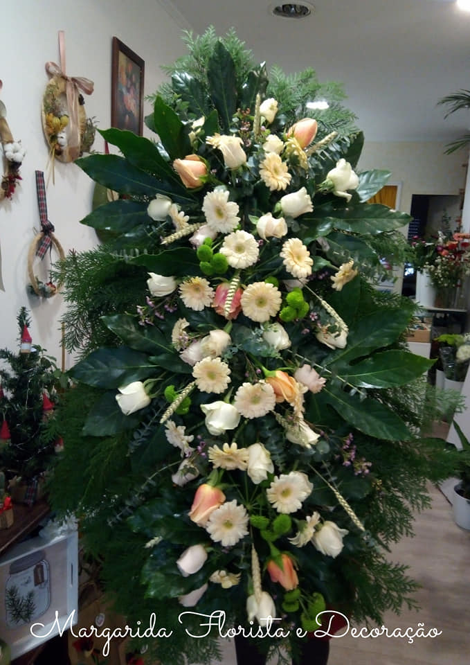 Arranjo floral vertical creme e pêssego com folhagem verde num interior de loja