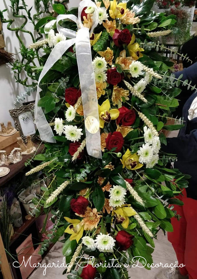 Arranjo floral vertical com rosas vermelhas, flores brancas e amarelas, folhas verdes e fita branca