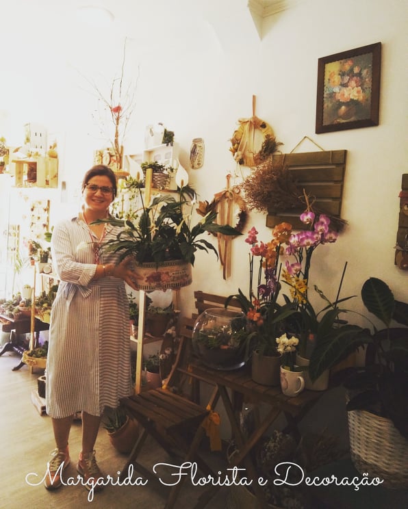mulher com vestido branco segurando planta em ambiente com várias plantas e decoração