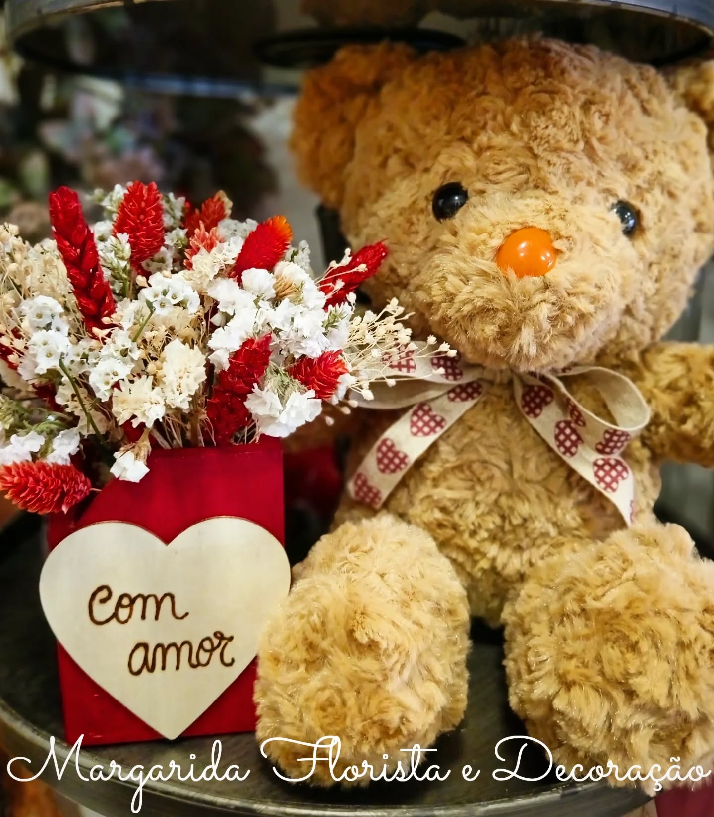 Urso de peluche com arranjo de flores secas e placa com texto
