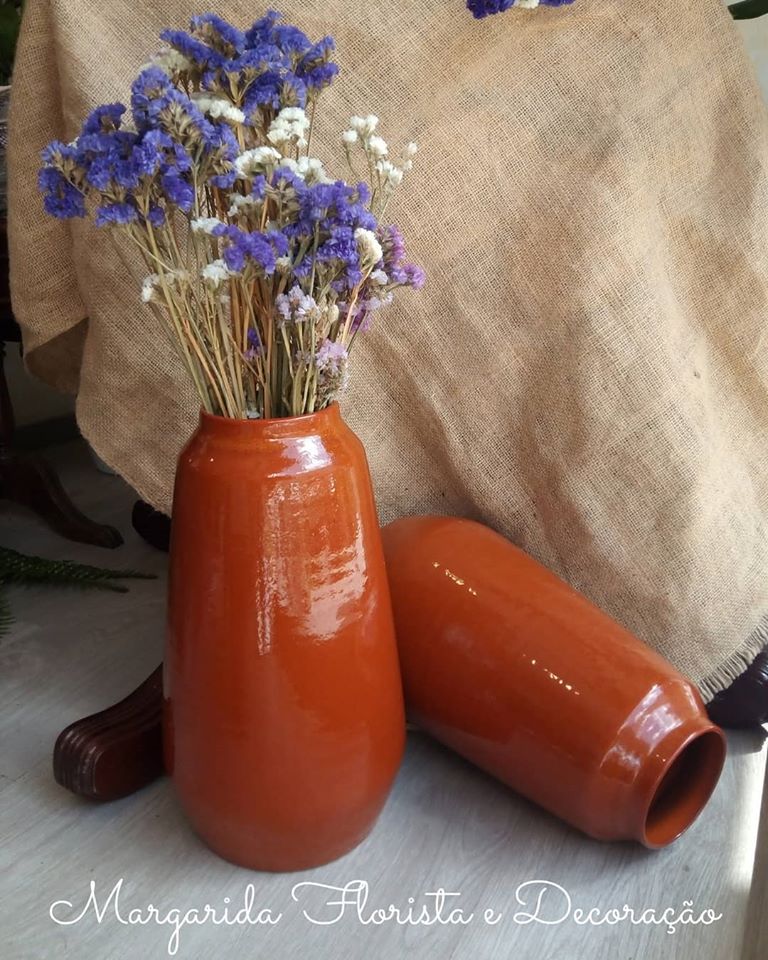 Dois vasos de cerâmica laranja com flores secas em fundo de tecido bege
