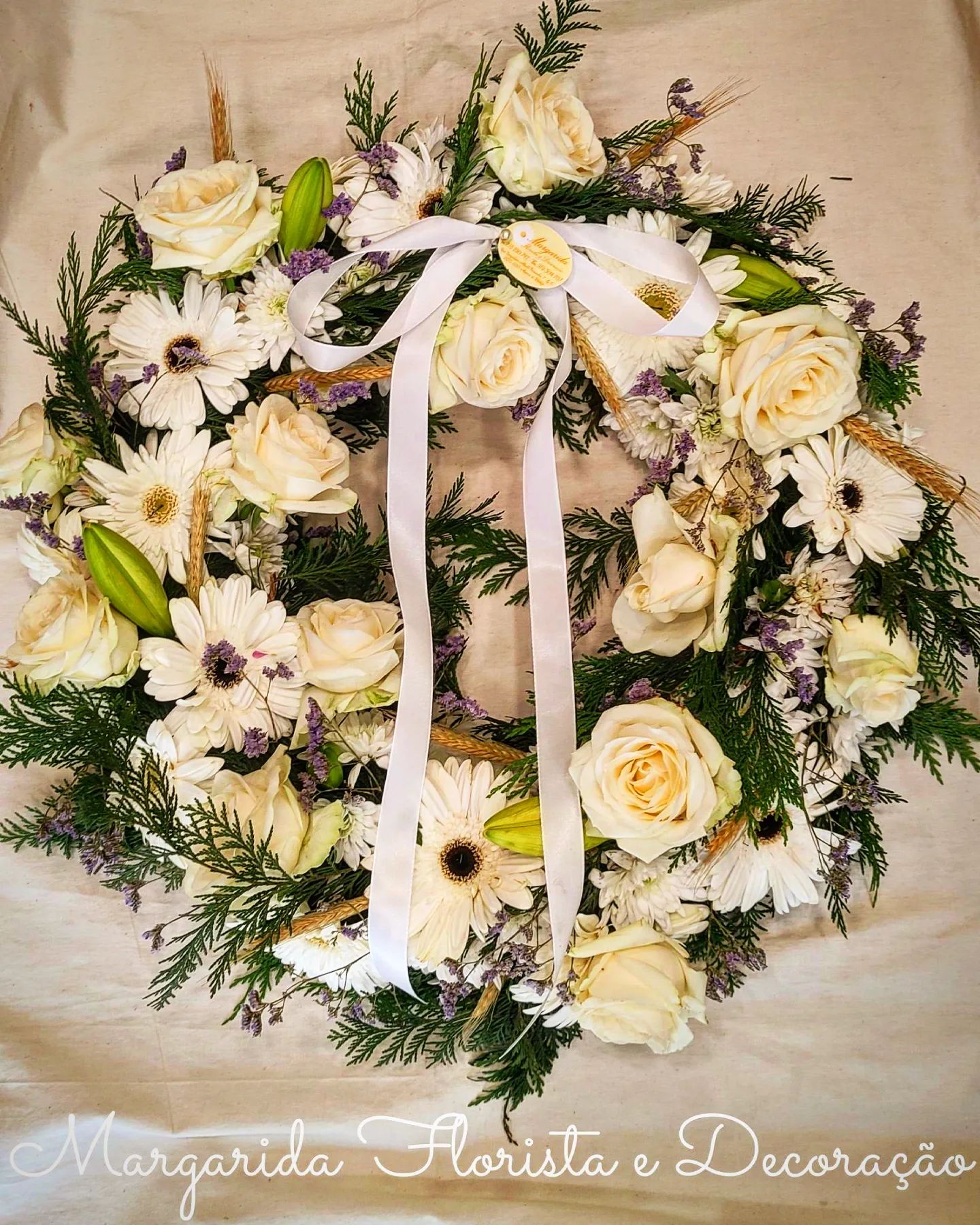 Coroa decorativa de flores brancas com fita branca sobre pano bege