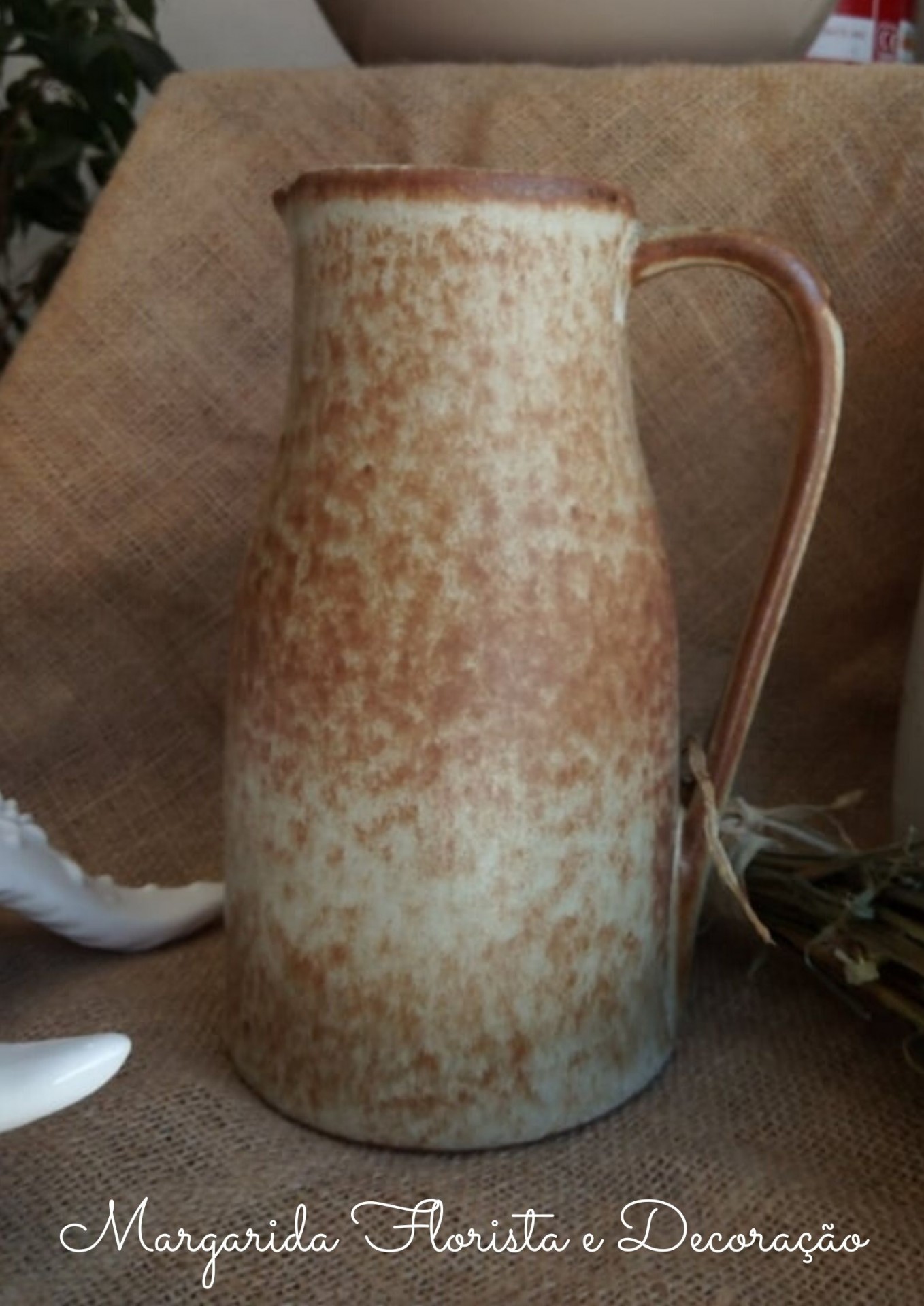 Jarro de cerâmica castanho e bege com textura irregular sobre juta