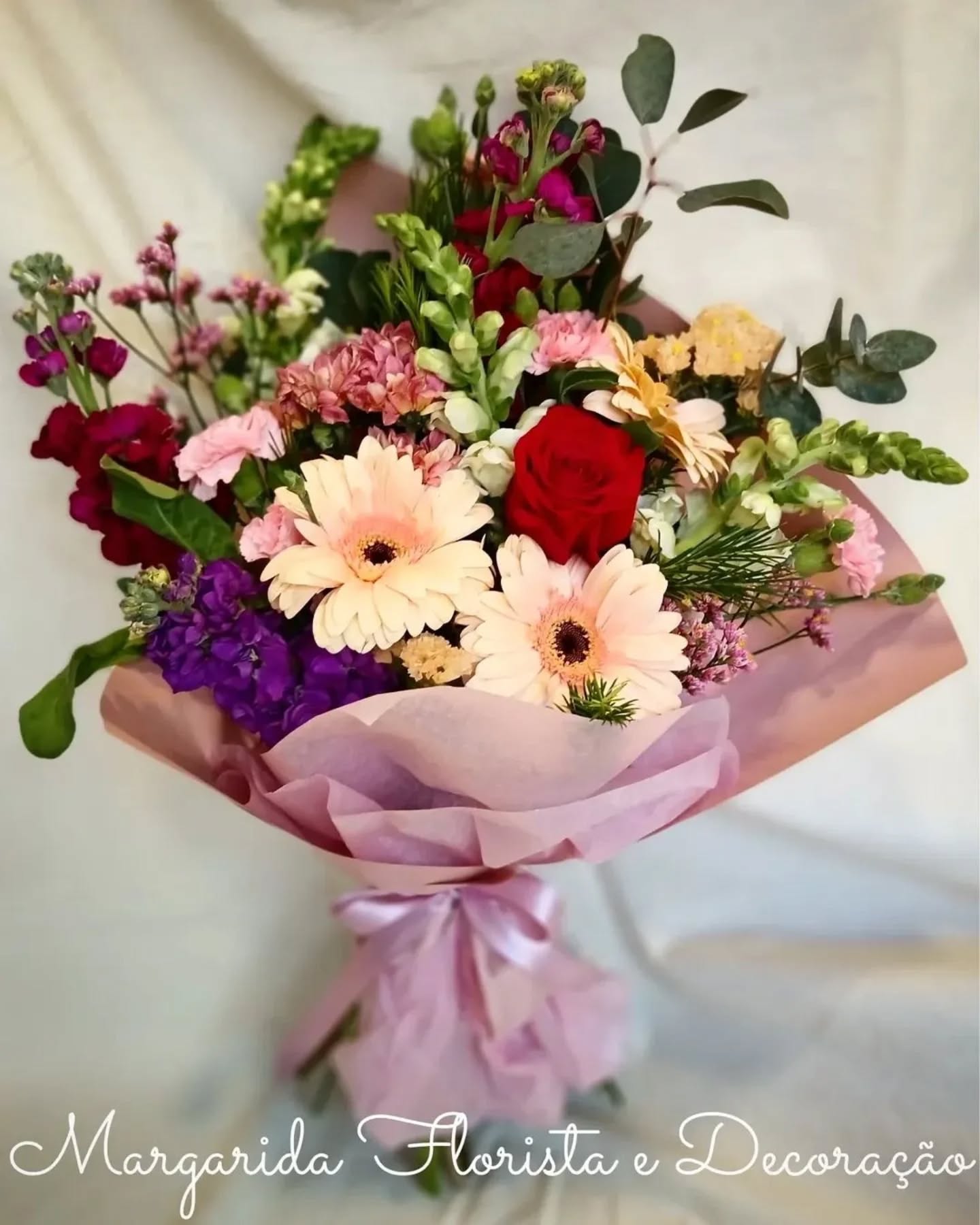 Bouquet de flores variadas em papel rosa claro com laço
