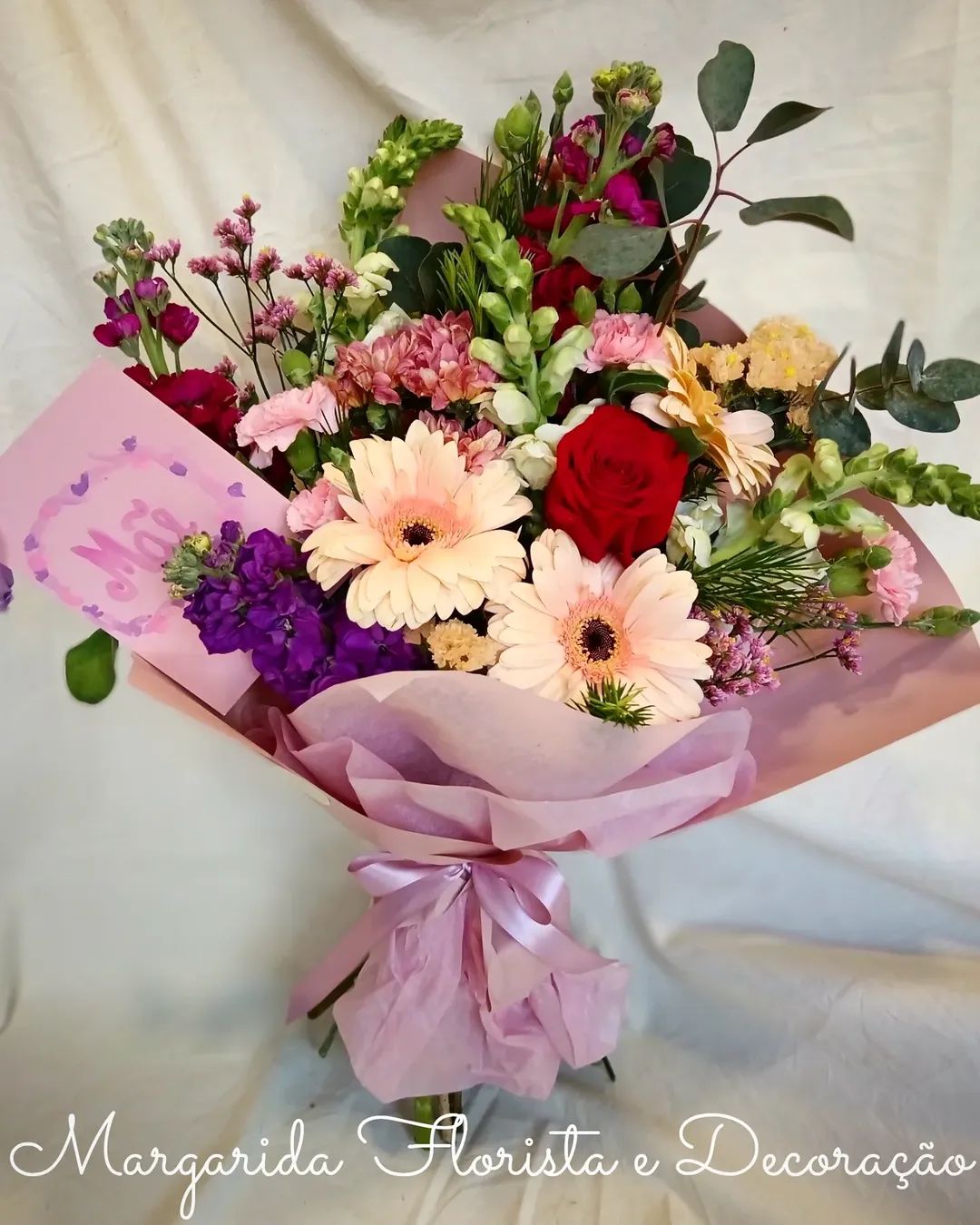 Buquê de flores coloridas em papel rosa com cartão escrito Mãe