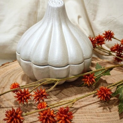 Frasco prateado em forma de alho com flores secas laranja sobre tábua de madeira