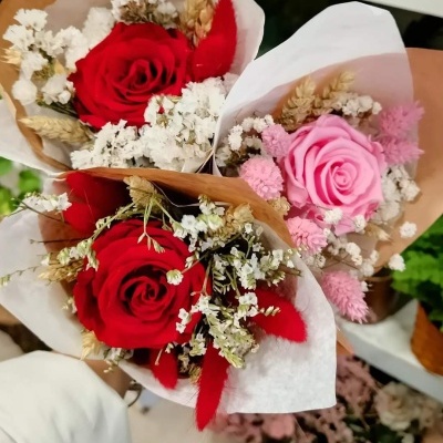Três pequenos bouquets de flores com rosas vermelhas e rosa, flores brancas pequenas e elementos secos decorativos.