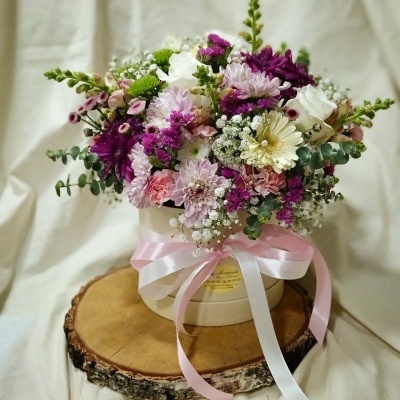 Arranjo floral colorido em caixa redonda creme com fita rosa e branca
