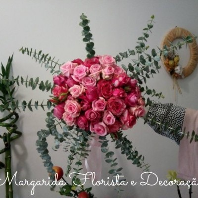 Bouquet grande de rosas rosa com folhagem verde prateada sendo segurado por uma mão