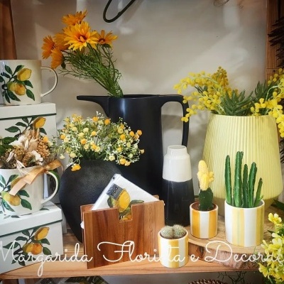 Canecas com limões, vasos e jarras com flores artificiais, cactos em vasos pequenos, arranjo decorativo em prateleira de madeira