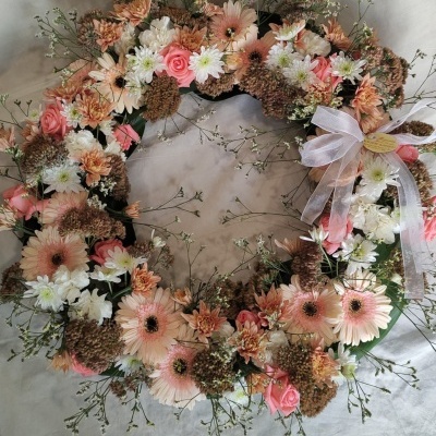 Coroa circular decorativa com flores em tons rosa, branco e castanho com laço branco.