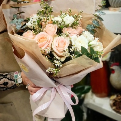 Bouquet de rosas cor-de-rosa claras e flores brancas com folhagem verde, embrulhado em papel bege com fita cor-de-rosa