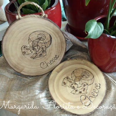 Tábuas de madeira redondas com gravuras de queijo e cogumelo e texto, ao lado de vasos de plantas vermelhos