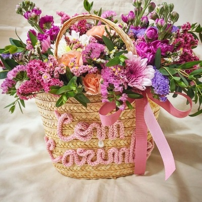 Cesto de palha com flores variadas e fita rosa
