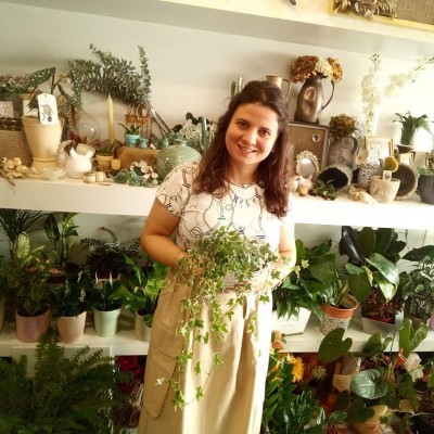 Mulher sorridente segura planta em loja com várias plantas e objetos decorativos