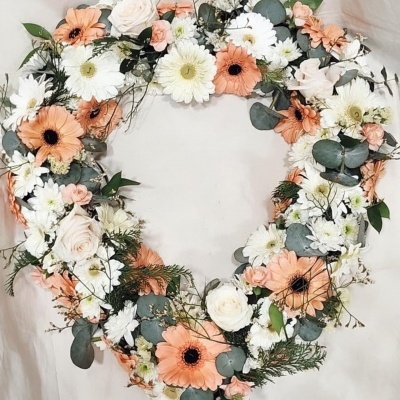 Coroa de flores artificiais branca, creme e laranja suave com folhas verdes e texto decorativo