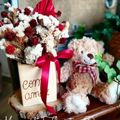 Arranjo de flores secas vermelhas e brancas com urso de pelúcia castanho claro num ambiente decorativo