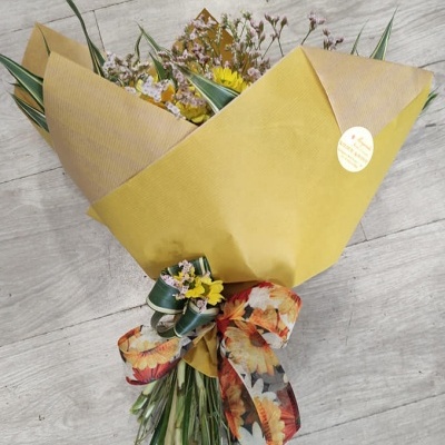 Bouquet de flores embalado em papel amarelo com laço floral