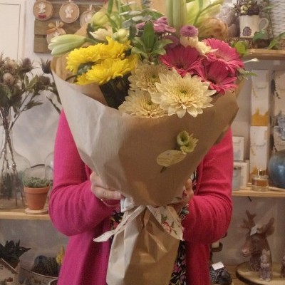Buquê de flores variadas em papel kraft segurado por pessoa em loja decorada