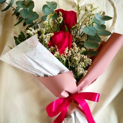Buquê de rosas vermelhas e folhagem embrulhado com papel rosa e branco com laço rosa