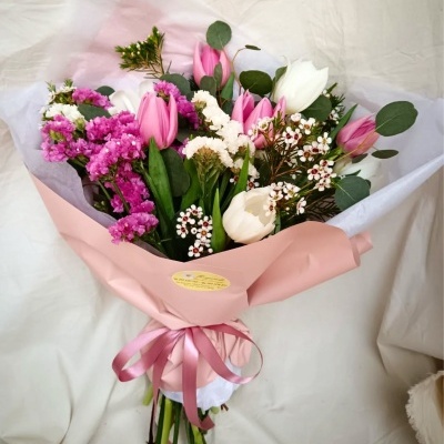 Buquê de flores com tulipas rosa e brancas e flores pequenas, embrulho rosa claro com fita