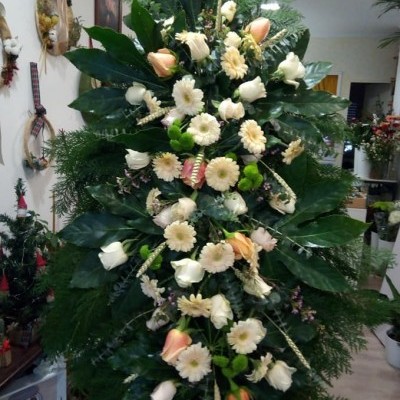 Arranjo floral vertical creme e pêssego com folhagem verde num interior de loja