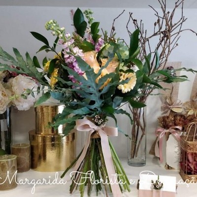 Ramo de flores coloridas com laço rosa numa mesa decorada com vasos e caixas