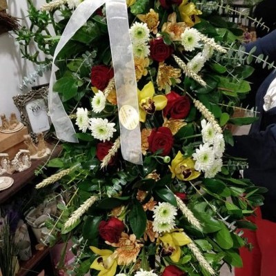Arranjo floral vertical com rosas vermelhas, flores brancas e amarelas, folhas verdes e fita branca