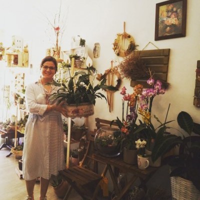 mulher com vestido branco segurando planta em ambiente com várias plantas e decoração