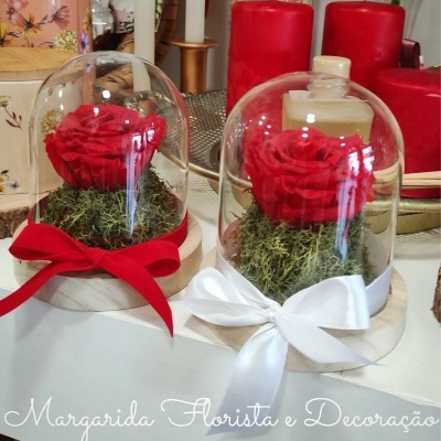 Dois arranjos florais com rosas vermelhas sob campânulas de vidro e fitas coloridas.
