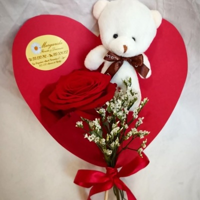 Arranjo com urso de peluche, rosa vermelha e flores brancas sobre coração vermelho