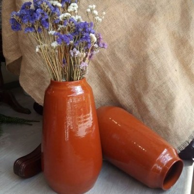 Dois vasos de cerâmica laranja com flores secas em fundo de tecido bege