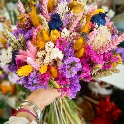 Buquê de flores secas multicolorido sendo segurado por uma mão com pulseiras