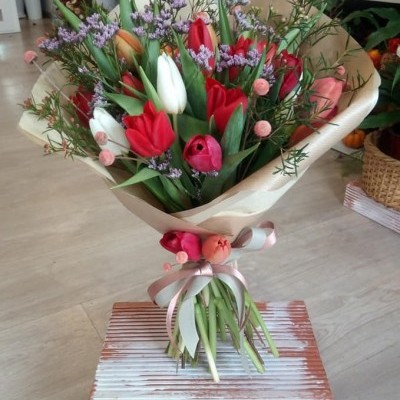 Bouquet de tulipas vermelhas e brancas com flores pequenas lilás e cor-de-rosa em papel castanho claro com fita rosa