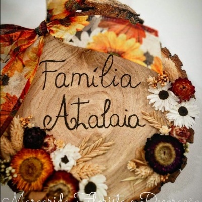 Placa decorativa de madeira com flores secas e laço laranja com texto 'Familia Atalaia'.