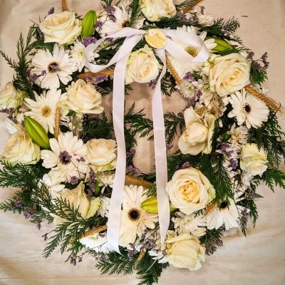 Coroa decorativa de flores brancas com fita branca sobre pano bege