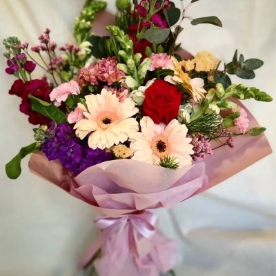 Bouquet de flores variadas em papel rosa claro com laço