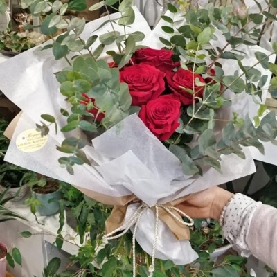 Buquê de rosas vermelhas e folhagem verde envolto em papel branco segurado pela mão de uma pessoa