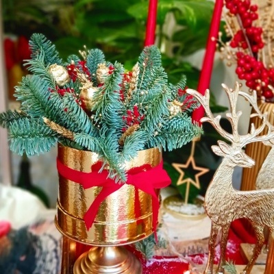 Arranjo decorativo de Natal com ramos verdes e vaso dourado.