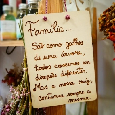 Placa decorativa de madeira com texto sobre família pendurada em suporte com flores secas ao lado