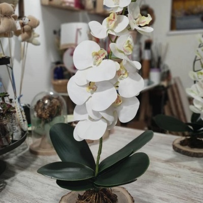 Orquídea artificial branca com folhas verdes em base de madeira sobre mesa em ambiente decorado