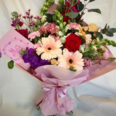 Buquê de flores coloridas em papel rosa com cartão escrito Mãe