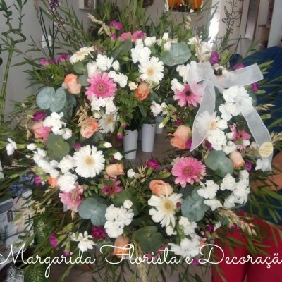 Coroa floral colorida com laço branco em ambiente interior com plantas.