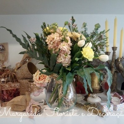 Arranjo de flores artificiais coloridas num vaso de vidro transparente sobre mesa decorada