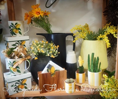 Canecas com limões, vasos e jarras com flores artificiais, cactos em vasos pequenos, arranjo decorativo em prateleira de madeira