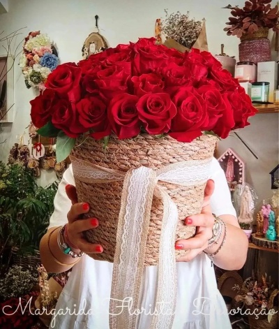 Cesto trançado com fita de renda e rosas vermelhas, decorado, segurado por pessoa.