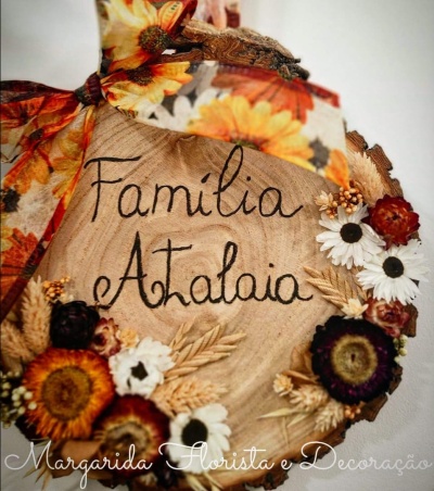 Placa decorativa de madeira com flores secas e laço laranja com texto 'Familia Atalaia'.