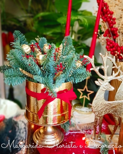 Arranjo decorativo de Natal com ramos verdes e vaso dourado.