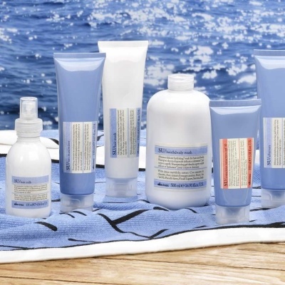 Produtos cosméticos em embalagens azuis e brancas sobre toalha azul à beira do mar.